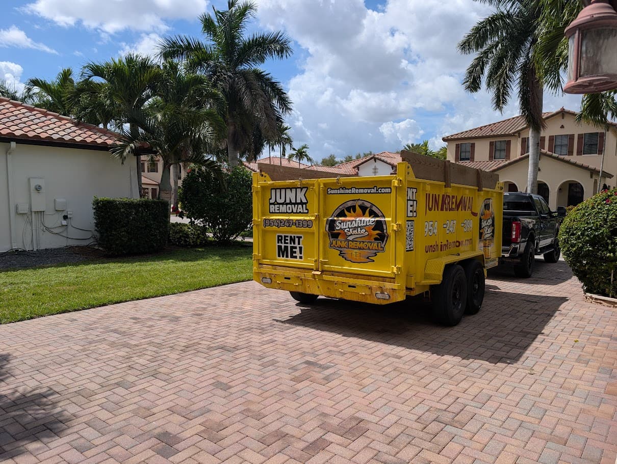 Yellow dump trailer hitched to a pickup truck on a herringbone paver driveway lined with palm trees