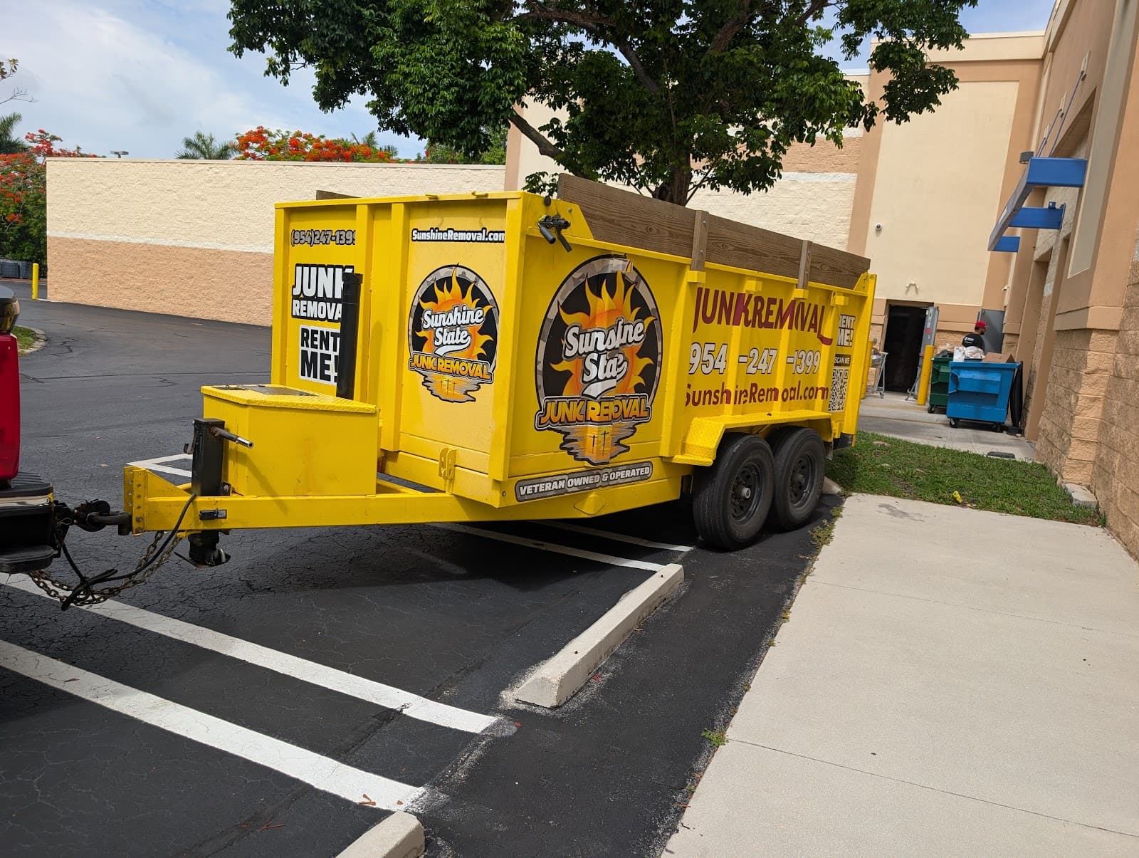Yellow dump trailer hitched to a truck in a parking lot behind a large commercial building