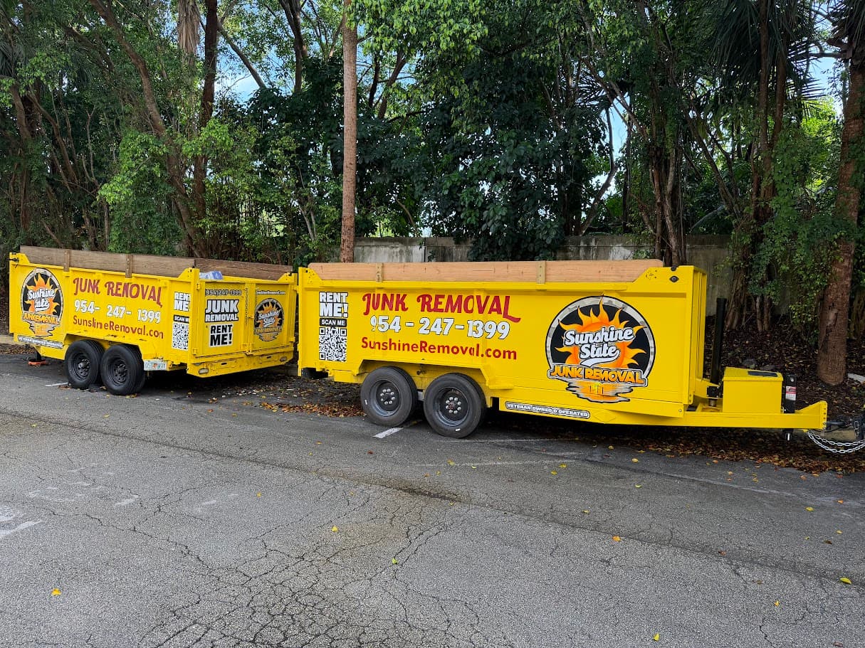 Two yellow dump trailers parked side by side in a lot with trees behind them