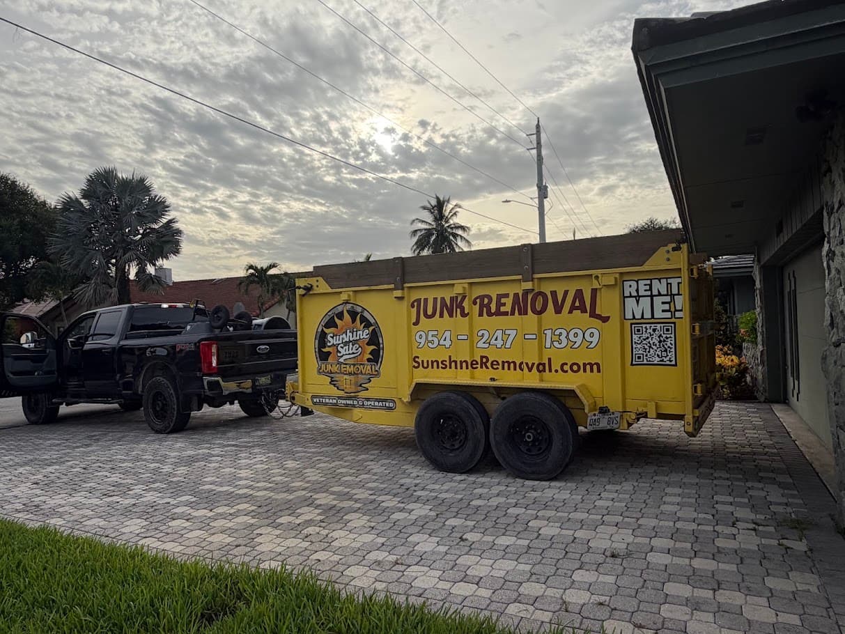 Yellow dump trailer hitched to a black pickup on a paver driveway beside a house at dawn
