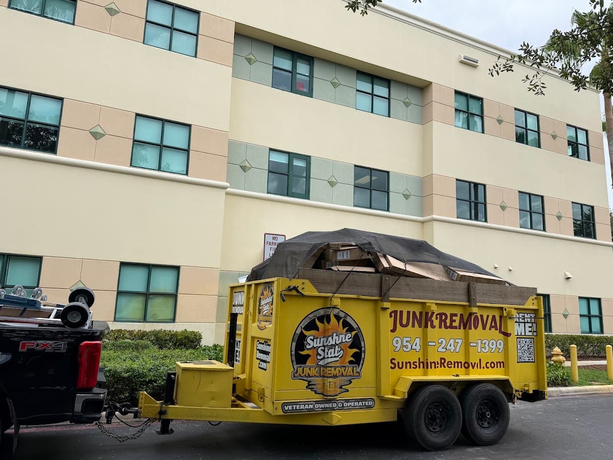 Yellow dump trailer loaded with tarped cardboard boxes outside a three-story building