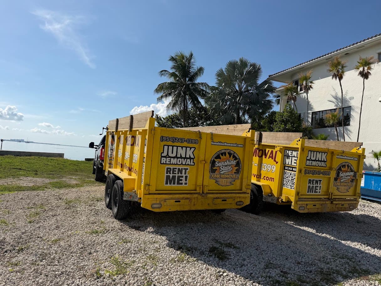 Two yellow dump trailers parked on gravel near the water beside a white building