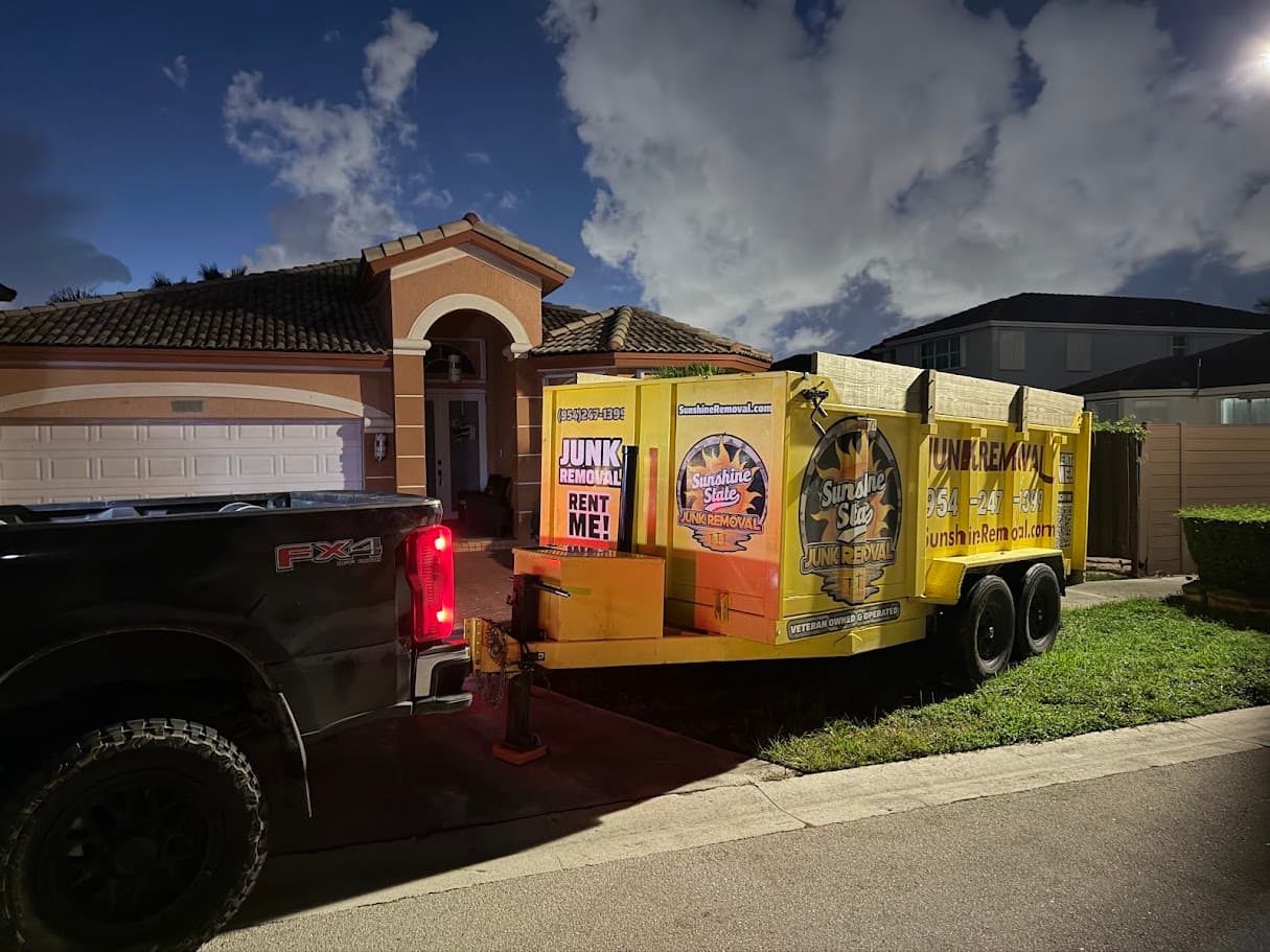 Yellow dump trailer hitched to a black pickup in front of a tile-roof home before sunrise
