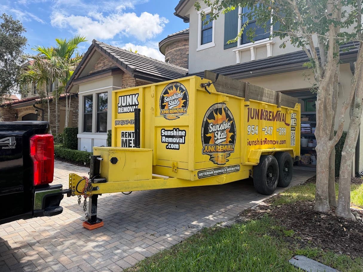 Yellow dump trailer hitched to a pickup on a paver driveway in front of a two-story home